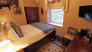 A bedroom with a bed, a wooden chair, a table with glasses, a TV, and a window with curtains.