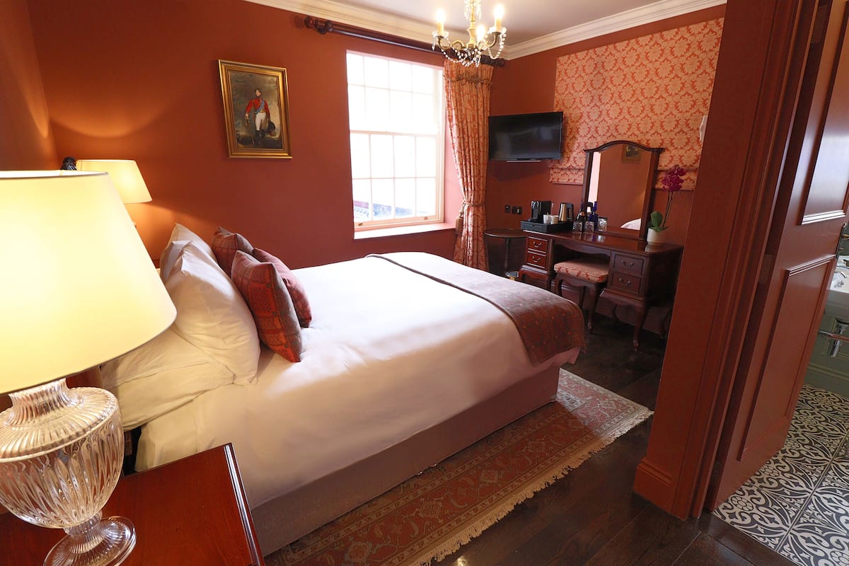 Una habitación de hotel con cama, escritorio, televisor y ventana con cortinas.