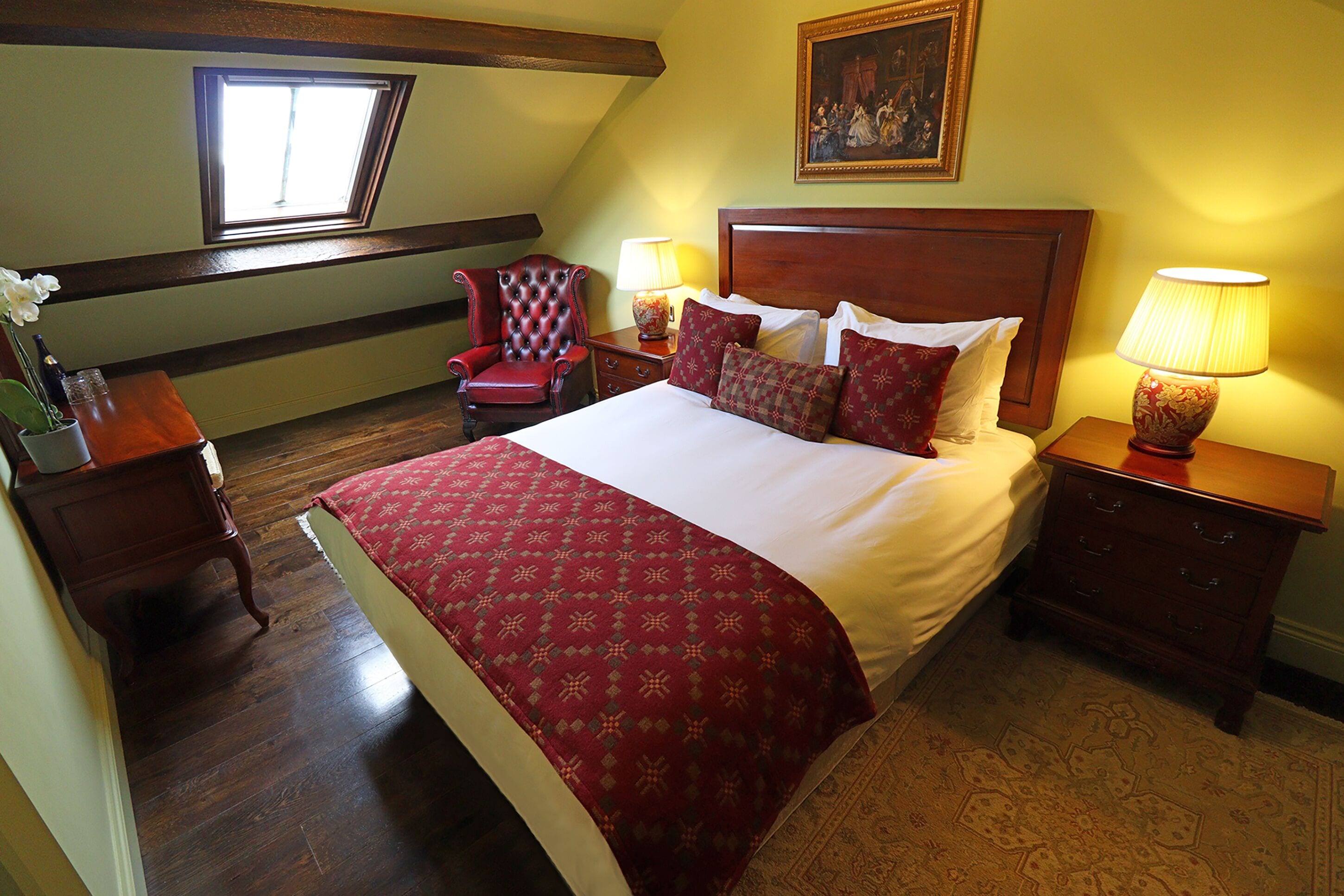 Un dormitorio con una cama grande, dos mesitas de noche con lámparas, un sillón rojo y una ventana con vistas.