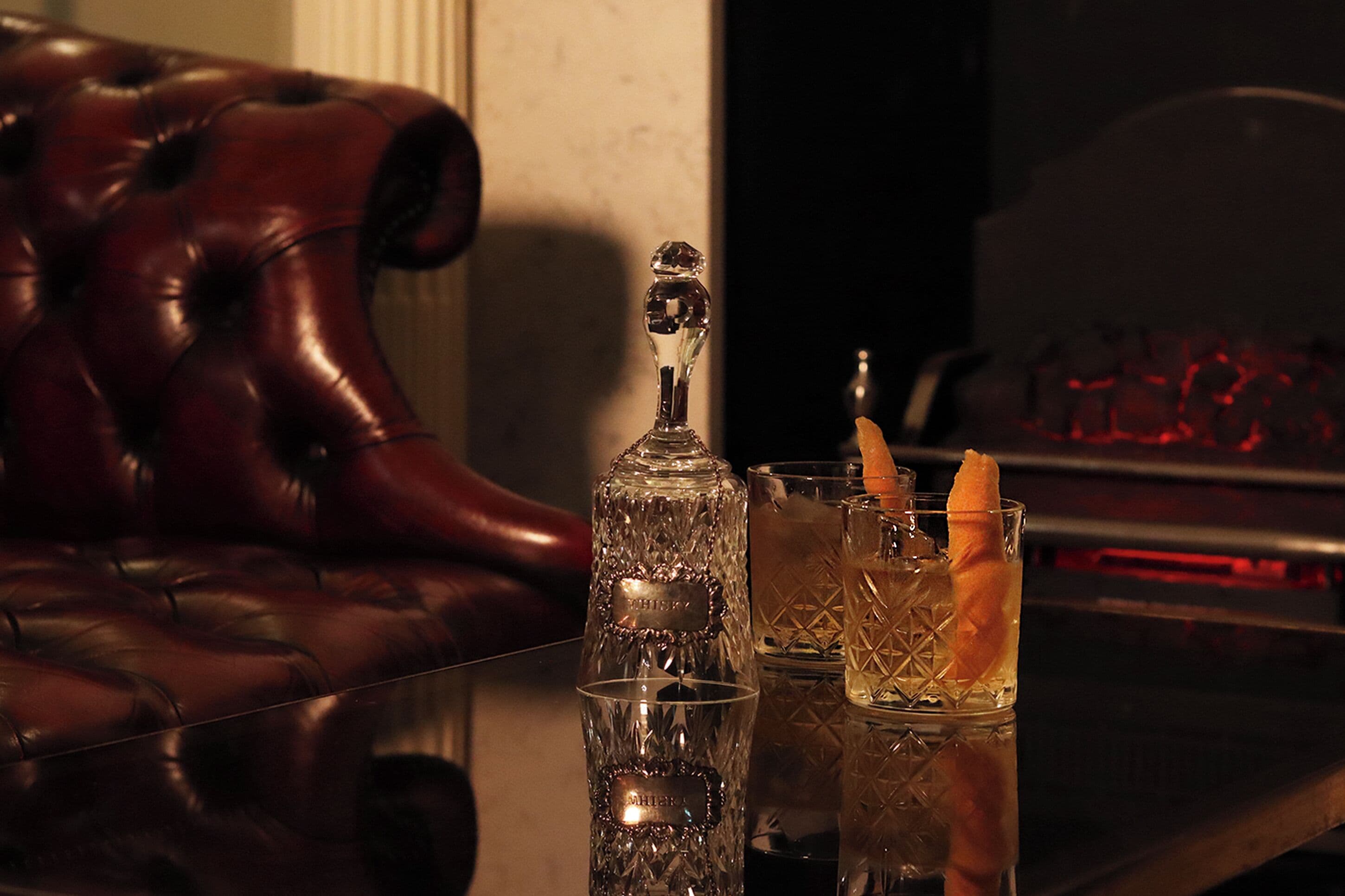 A bar area with a leather couch, a crystal decanter, and two glasses with a cocktail garnish.
