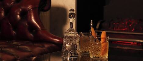 A bar area with a leather couch, a crystal decanter, and two glasses with a cocktail garnish.
