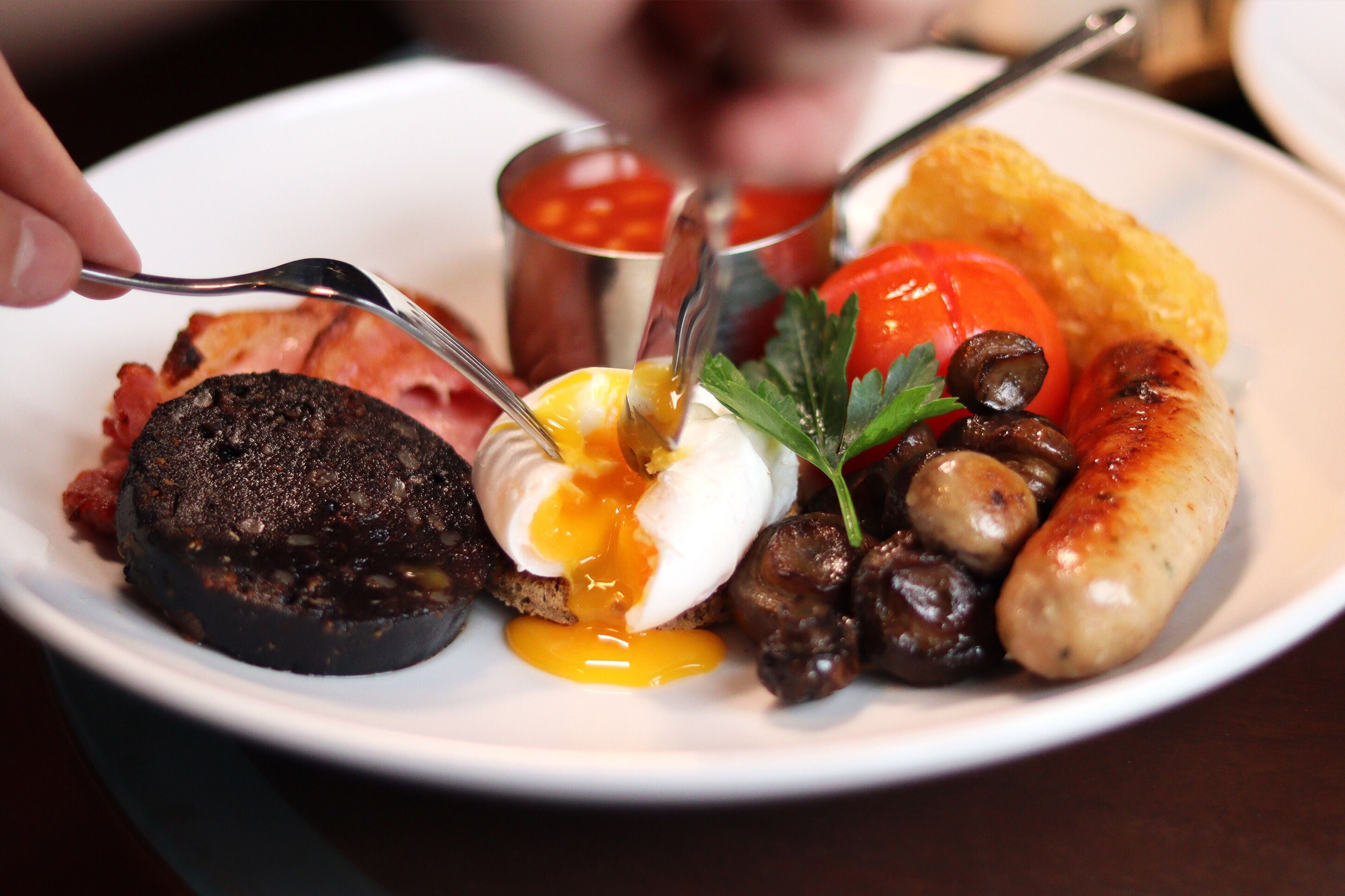 A plate of food with various items including a poached egg, mushrooms, sausages, and a slice of black pudding.