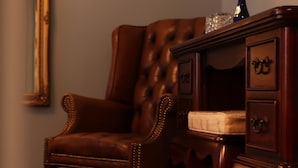 A brown leather armchair with a tufted backrest and a wooden side table with drawers.
