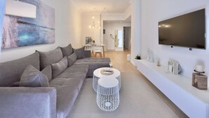 A modern living room with a grey sofa, a white coffee table, and a flat-screen TV mounted on the wall. - Tiramisu: Elegant apartment near Agia Sofia (Thessaloniki)