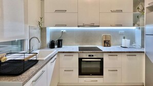 A modern kitchen with white cabinets, a built-in oven, a coffee maker, and a knife block. - Tiramisu: Elegant apartment near Agia Sofia (Thessaloniki)