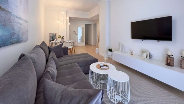 A modern living room with a grey sectional sofa, a round coffee table, and a flat-screen TV mounted on the wall. - Tiramisu: Elegant apartment near Agia Sofia (Thessaloniki)