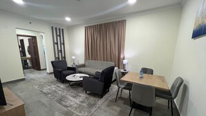 A modern living room with a sofa, armchairs, a coffee table, and a dining table with chairs. - Terminal Inn Airport Hotel & Apartment (Doha)