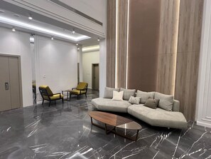 A modern living room with a sectional sofa, two armchairs, a coffee table, and a large wooden accent wall. - Terminal Inn Airport Hotel & Apartment (Doha)