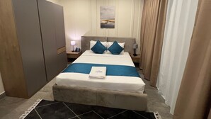 A hotel room with a bed, a nightstand, a lamp, a painting on the wall, and a wardrobe. - Terminal Inn Airport Hotel & Apartment (Doha)