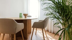 Un comedor con una mesa redonda de madera, dos sillas color beige, un jarrón verde y un cuenco.