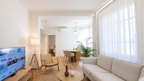 Una sala de estar moderna con un televisor de pantalla plana, un sofá, una mesa de centro y un comedor con sillas.
