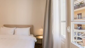 Habitación de hotel con cama, mesita de noche y vistas a un balcón con mobiliario exterior.