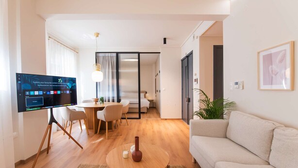Un salon moderne doté d’un téléviseur à écran plat, d’une table basse ronde en bois, d’un canapé beige et d’un coin repas avec une table et des chaises.