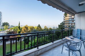 Un balcon avec une table et des chaises, donnant sur un paysage urbain composé d’immeubles et d’une étendue d’eau.