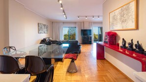 A modern living room with a glass dining table, black chairs, a sofa, and a TV. - City Moon: Chic apt with park and sea view (Thessaloniki)