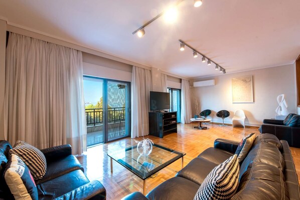 Un salon moderne avec une table basse en verre, des canapés en cuir, un téléviseur à écran plat et un balcon avec vue.