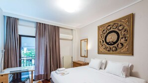 A hotel room with a bed, a desk, a chair, a window with curtains, and a decorative wall piece. - City Moon: Chic apt with park and sea view (Thessaloniki)