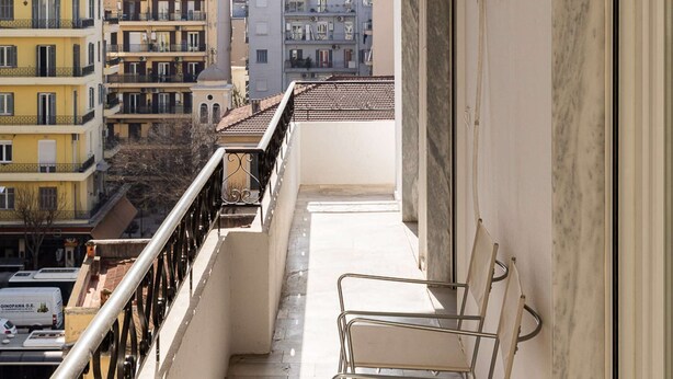 Ein Balkon mit Metallstühlen, gefliestem Boden und Blick auf Stadtgebäude.