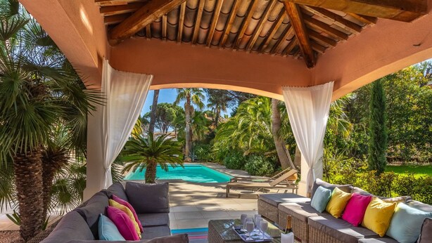 A covered outdoor seating area with wicker furniture, a pool in the background, and lush greenery. - Vacation home Indigo by Interhome (Grimaud)
