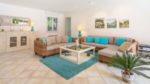 A spacious living room with a beige sofa, a glass coffee table, and a teal rug. There are two lamps, a mirror, and a cabinet with glass doors. - Vacation home Indigo by Interhome (Grimaud)
