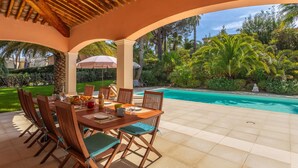 An outdoor dining area with a pool, covered by a wooden pergola, surrounded by lush greenery. - Vacation home Indigo by Interhome (Grimaud)
