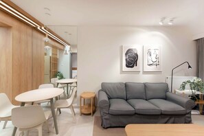 A modern living room with a grey sofa, white chairs, a small round table, and two abstract art pieces on the wall.