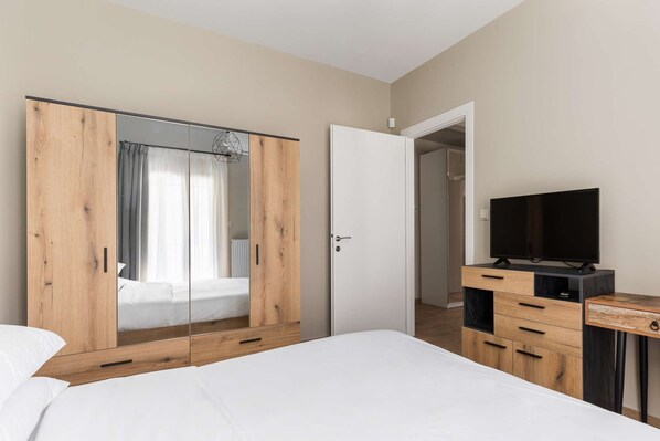 A bedroom with a bed, a wardrobe, a television, and a door leading to another room.