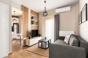 Una sala de estar moderna con un sofá gris, un televisor, un separador de madera y un comedor con una mesa y sillas.