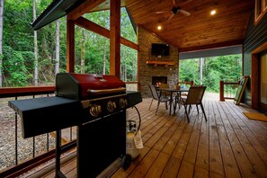 Una terraza de madera con una parrilla, una chimenea de piedra y una mesa con sillas.