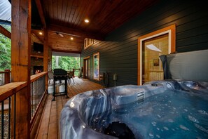 Una terraza de madera con jacuzzi, mobiliario exterior y una chimenea de piedra.
