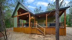 A cabin with a wooden deck, a staircase, and a large window overlooking the forest. - Moonlight Ridge-Loft/Privacy/HotTub (Broken Bow)