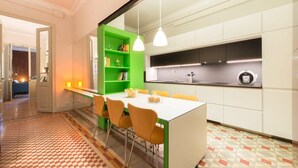 Eine moderne Küche mit weißer Arbeitsplatte, grünen Regalen und orangefarbenen Stühlen.