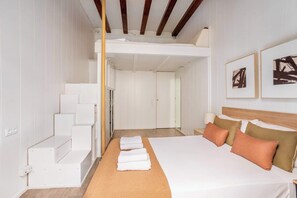 A hotel room with a bunk bed, a neatly made bed with towels, a headboard with pillows, and artwork on the wall. - Paseo de Gracia modern 4BD with Terrace (Barcelona)