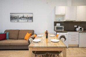Un ambiente compatto con un tavolo da pranzo per quattro persone, un divano con cuscini, una lavatrice e un forno a microonde.