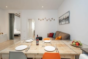 Uma sala de jantar com uma mesa de madeira posta para quatro pessoas, uma garrafa de vinho e um prato de frutas ao lado.