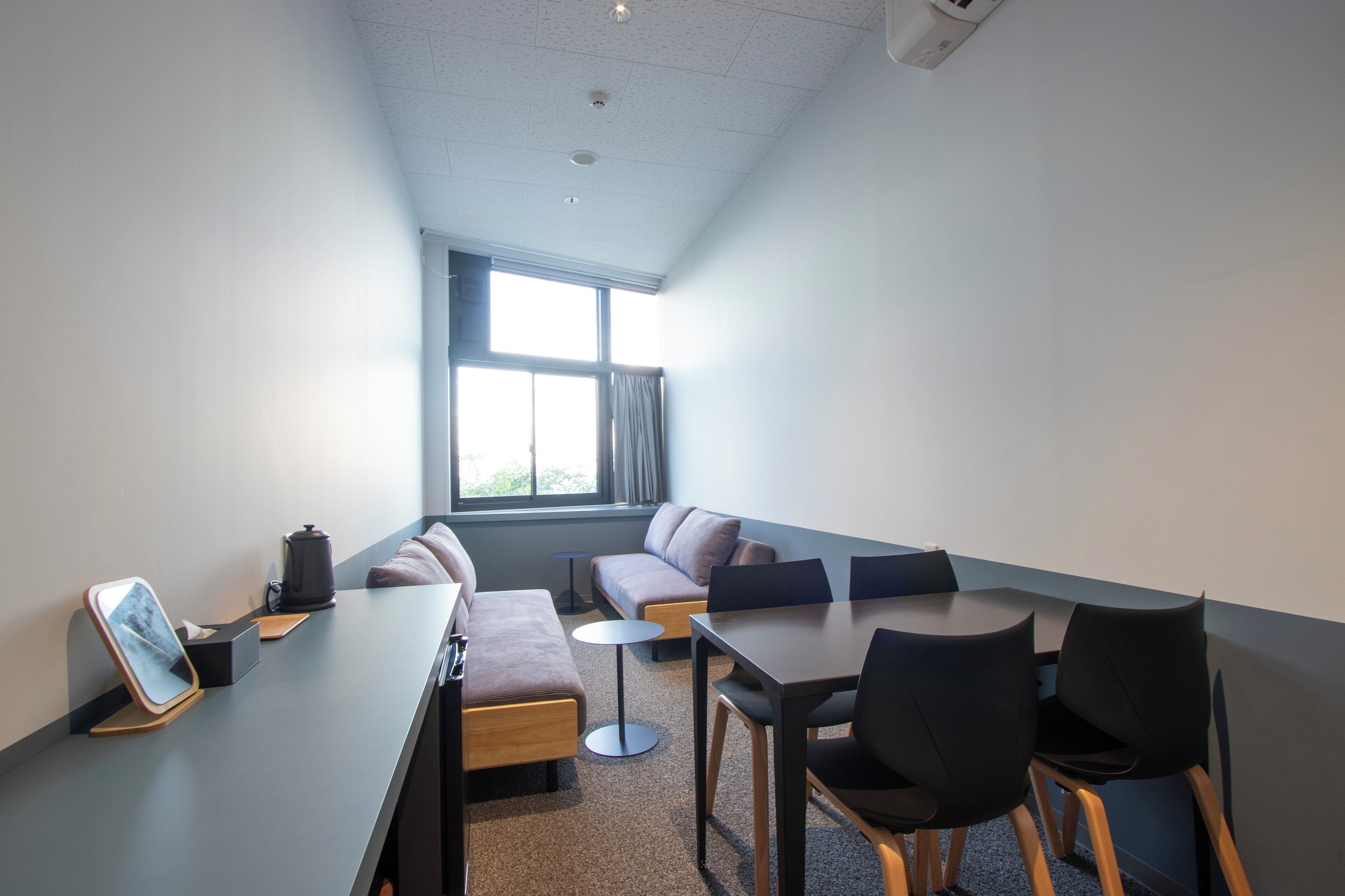 A modern meeting room with a long table, chairs, a sofa, and a coffee machine.