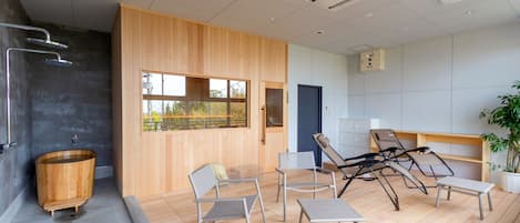 Une salle de spa moderne avec une baignoire en bois, un coin salon et de grandes fenêtres.