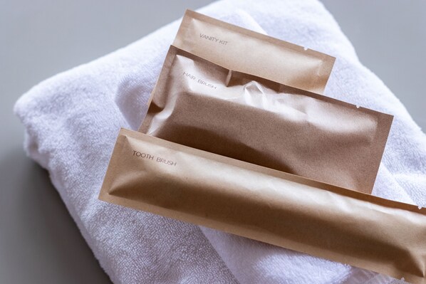 Three brown paper bags labeled 'VANITY KIT,' 'HAIR BRUSH,' and 'TOOTH BRUSH' on a white towel. - SAKIA STAY (Awaji)