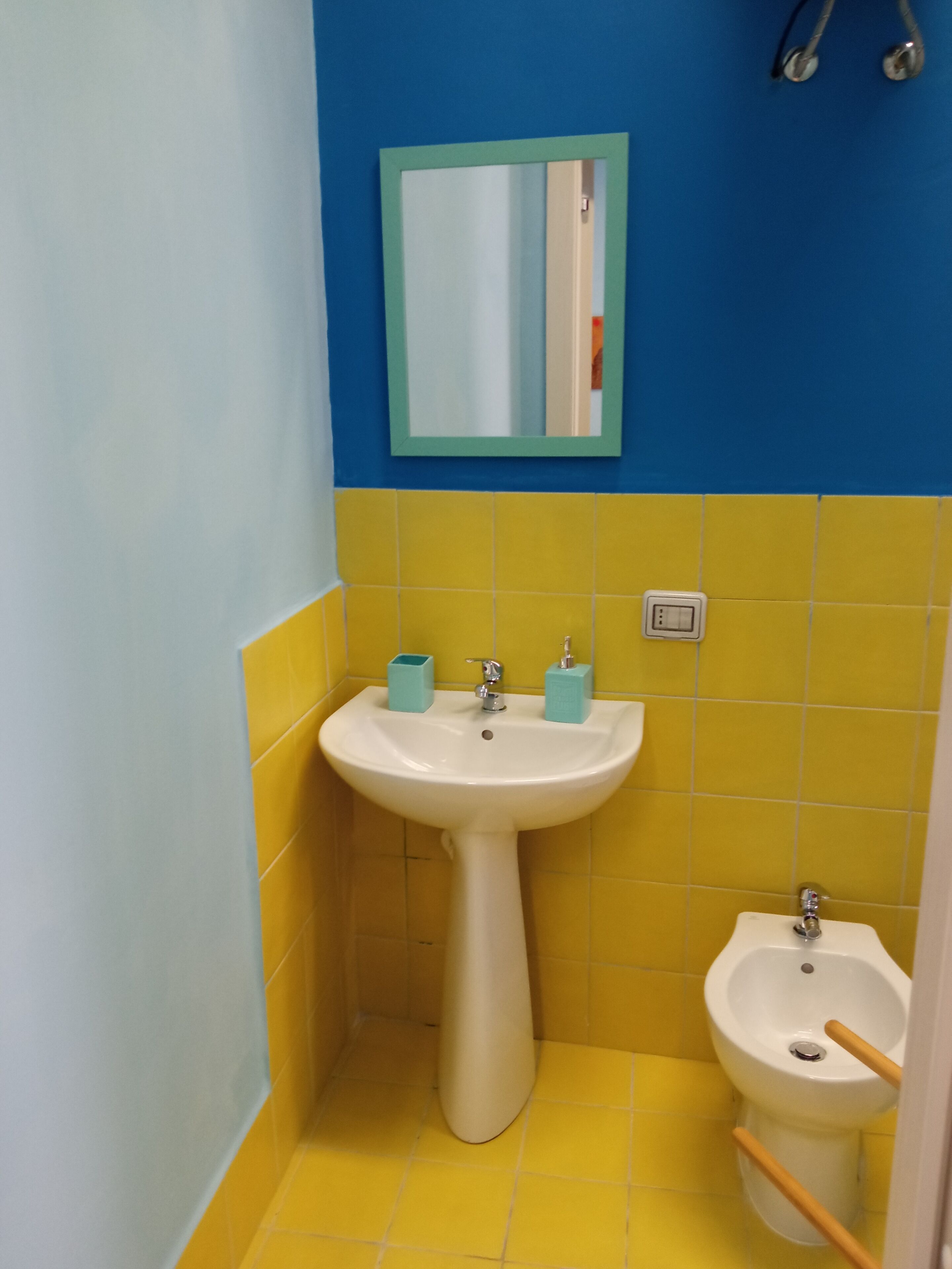 A bathroom with a white sink, a mirror, and a bidet. The walls are painted yellow and blue.