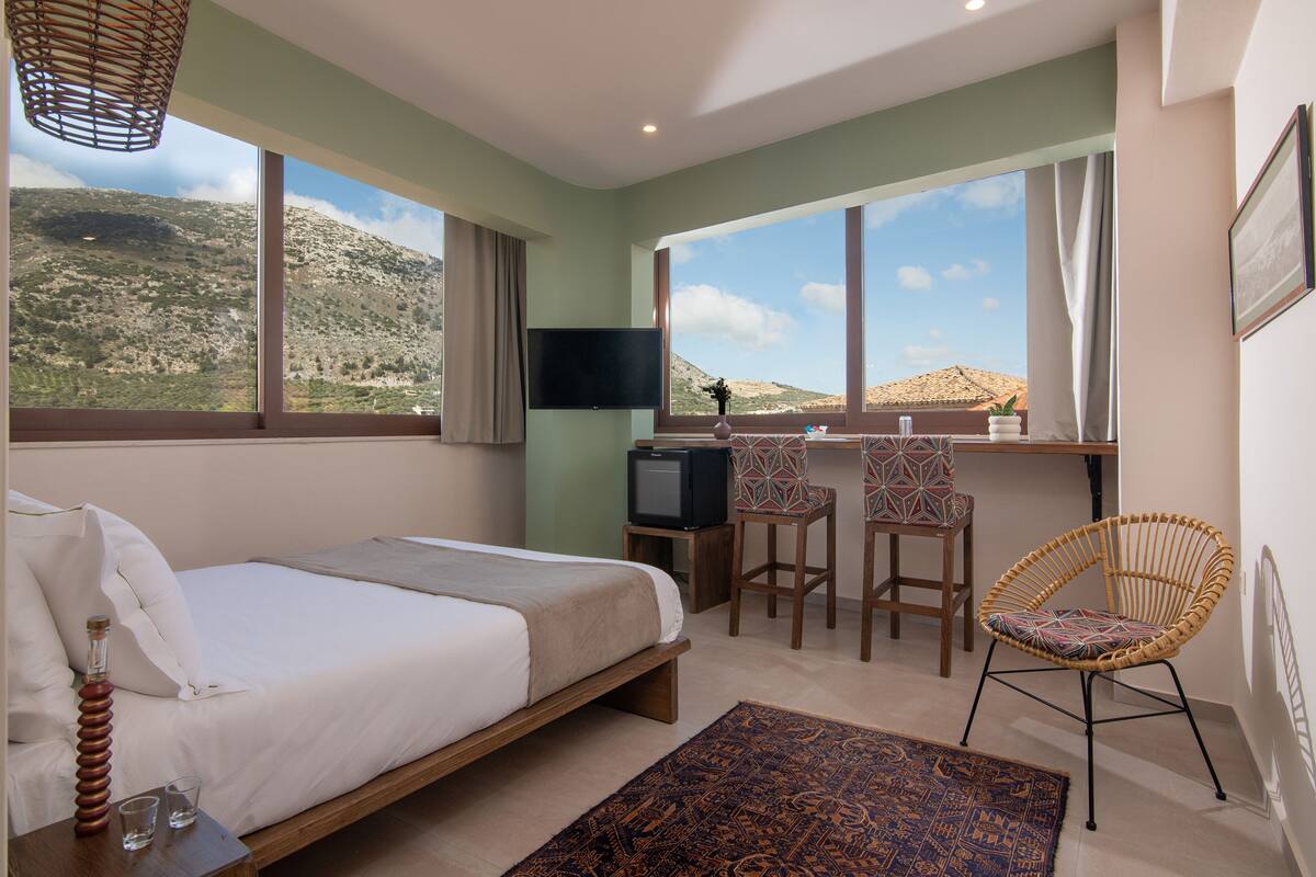 Un dormitorio con cama, escritorio, dos sillas, televisión y vista a un paisaje montañoso.