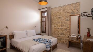 Un dormitorio con cama, mesita de noche, cómoda, espejo y pared de piedra.