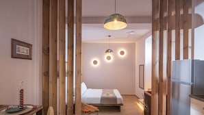 Una habitación de hotel moderna con cama, detalles de madera, una zona de comedor con mesa y sillas, y un refrigerador.