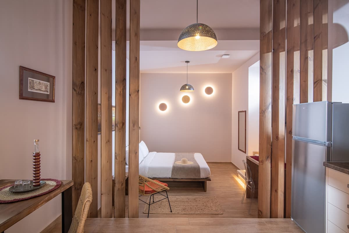 Una habitación de hotel moderna con cama, detalles de madera, una zona de comedor con mesa y sillas, y un refrigerador.