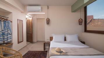 A bedroom with a bed, a hanging light fixture, a mirror, a wardrobe, and a window with a view of buildings.