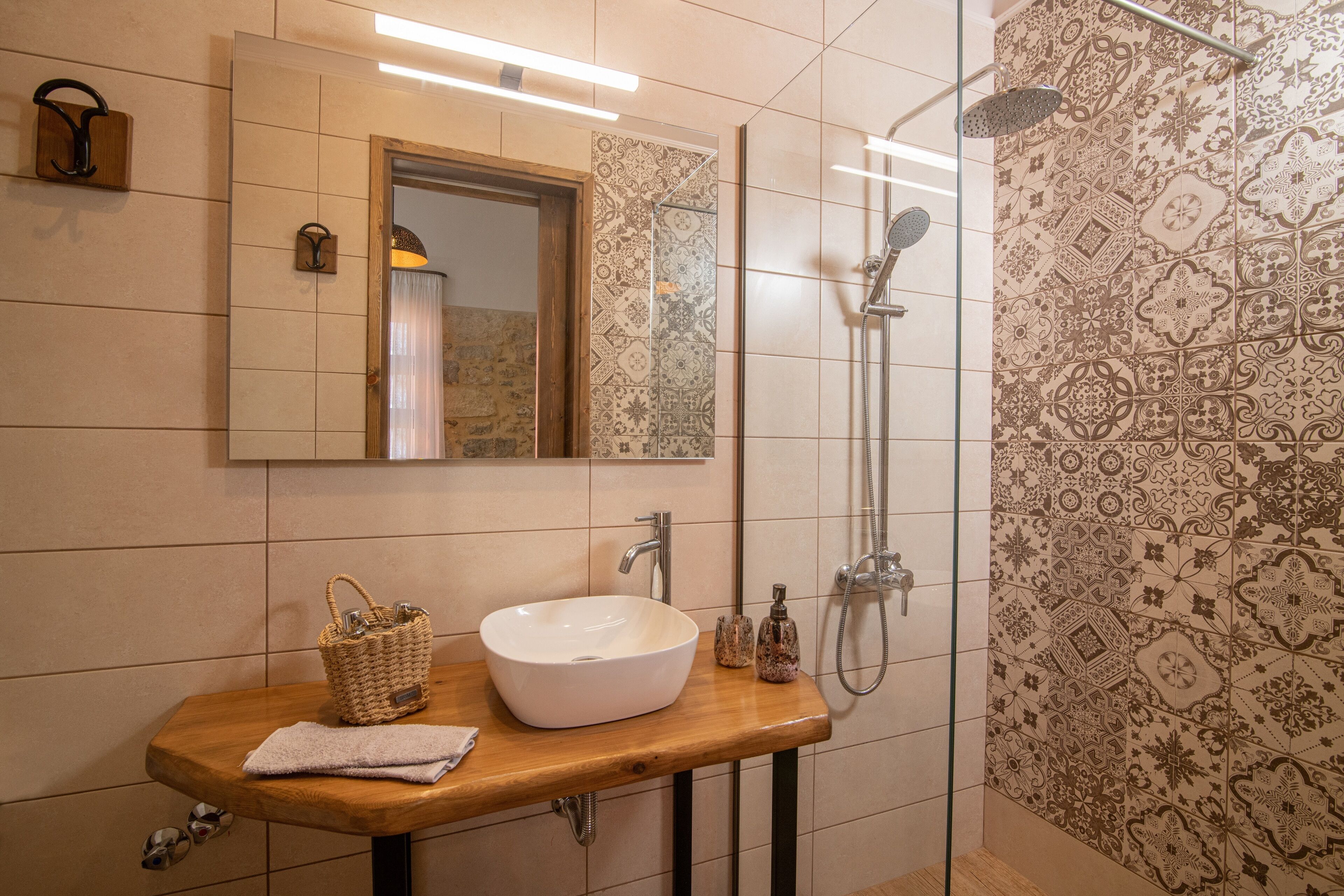 Ein Badezimmer mit einem Holzbidet, einem weißen Waschbecken, einem Spiegel und gemusterten Fliesen.