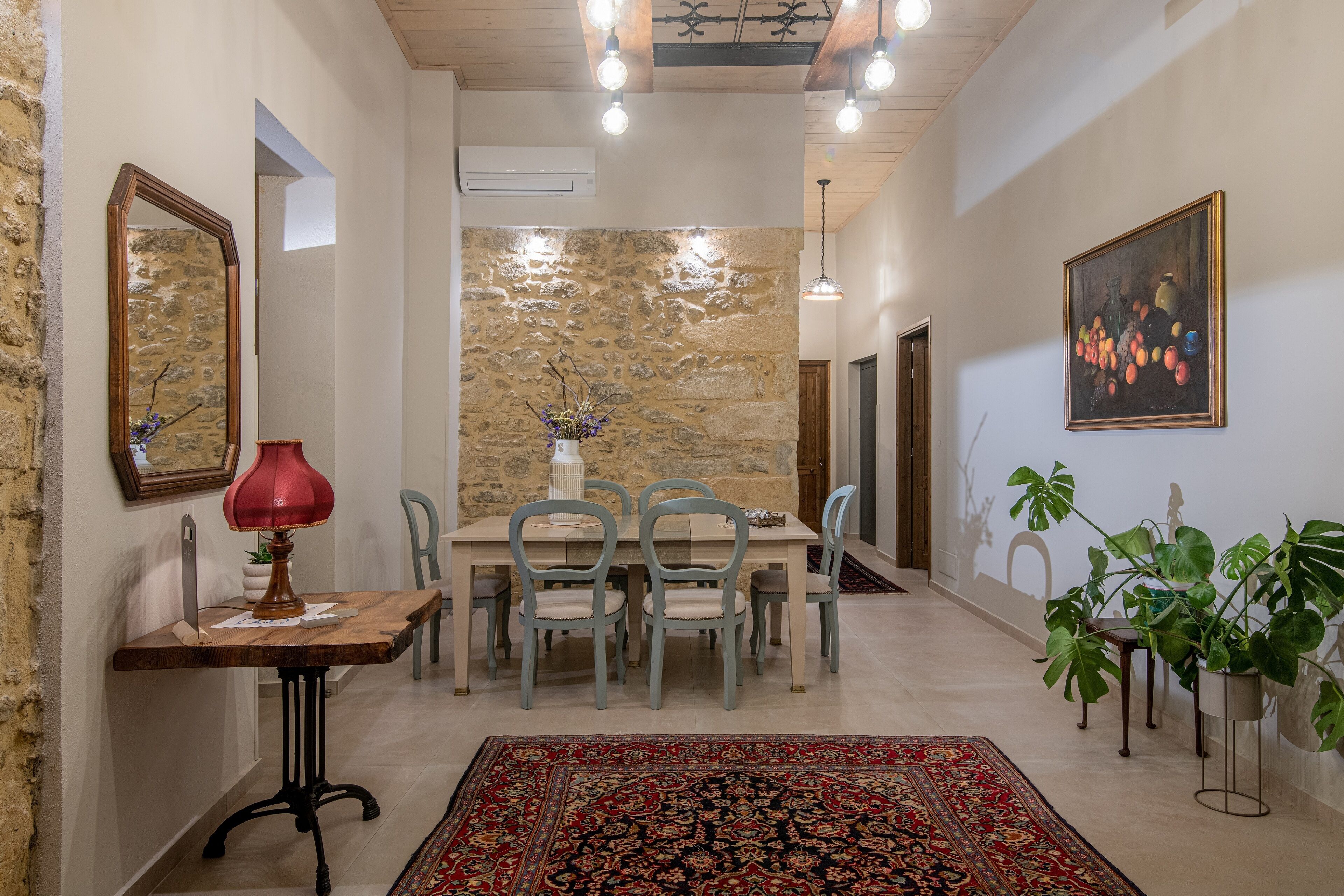 A dining area with a stone wall, a table with chairs, a red lamp, and a painting.