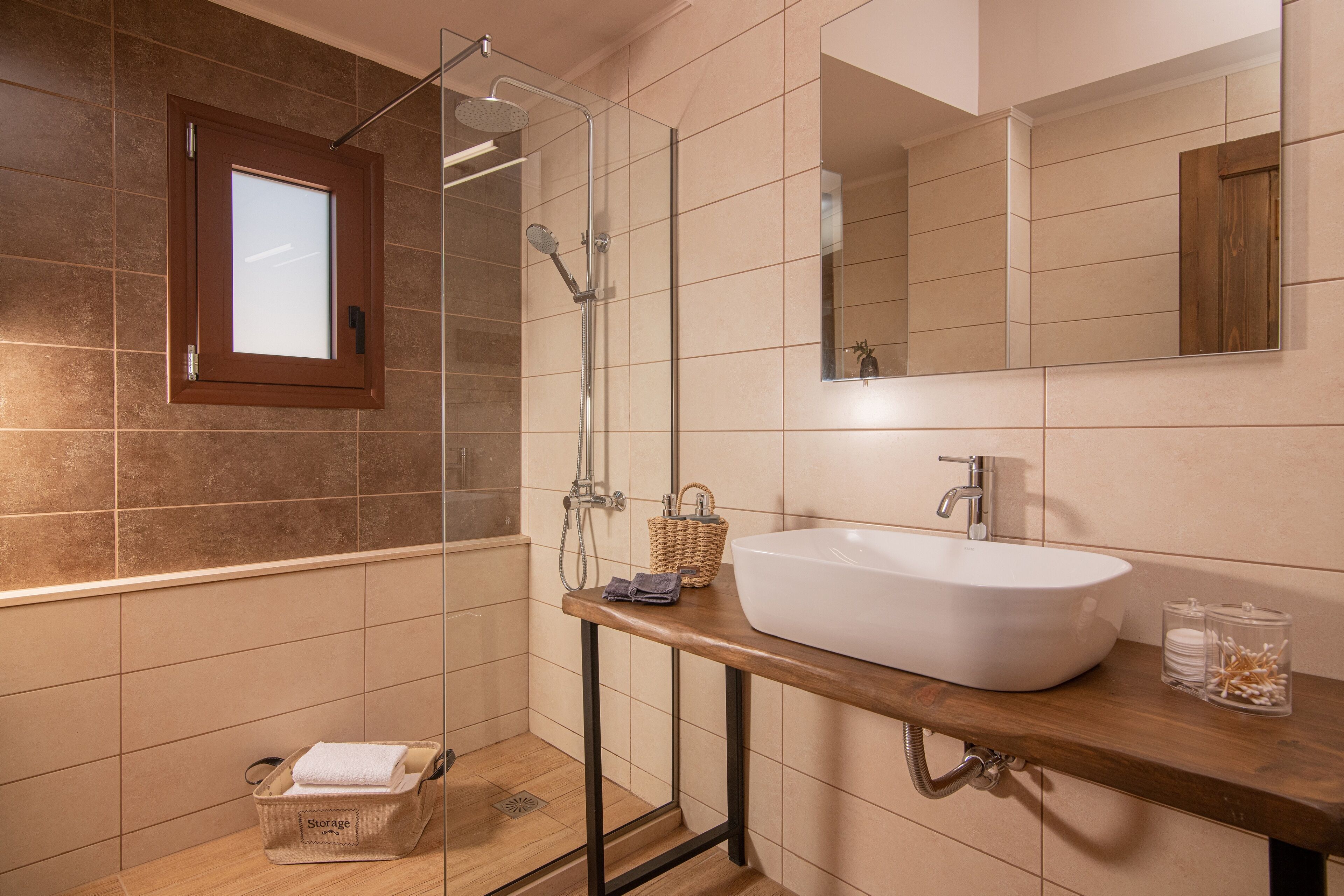 Een moderne badkamer met een douche in glazen cabine, een houten wastafelmeubel met een witte wasbak en een spiegel boven de wasbak.