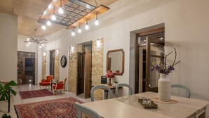 Un área de comedor con una mesa, sillas y una alfombra roja. Hay puertas de madera y un espejo en la pared.