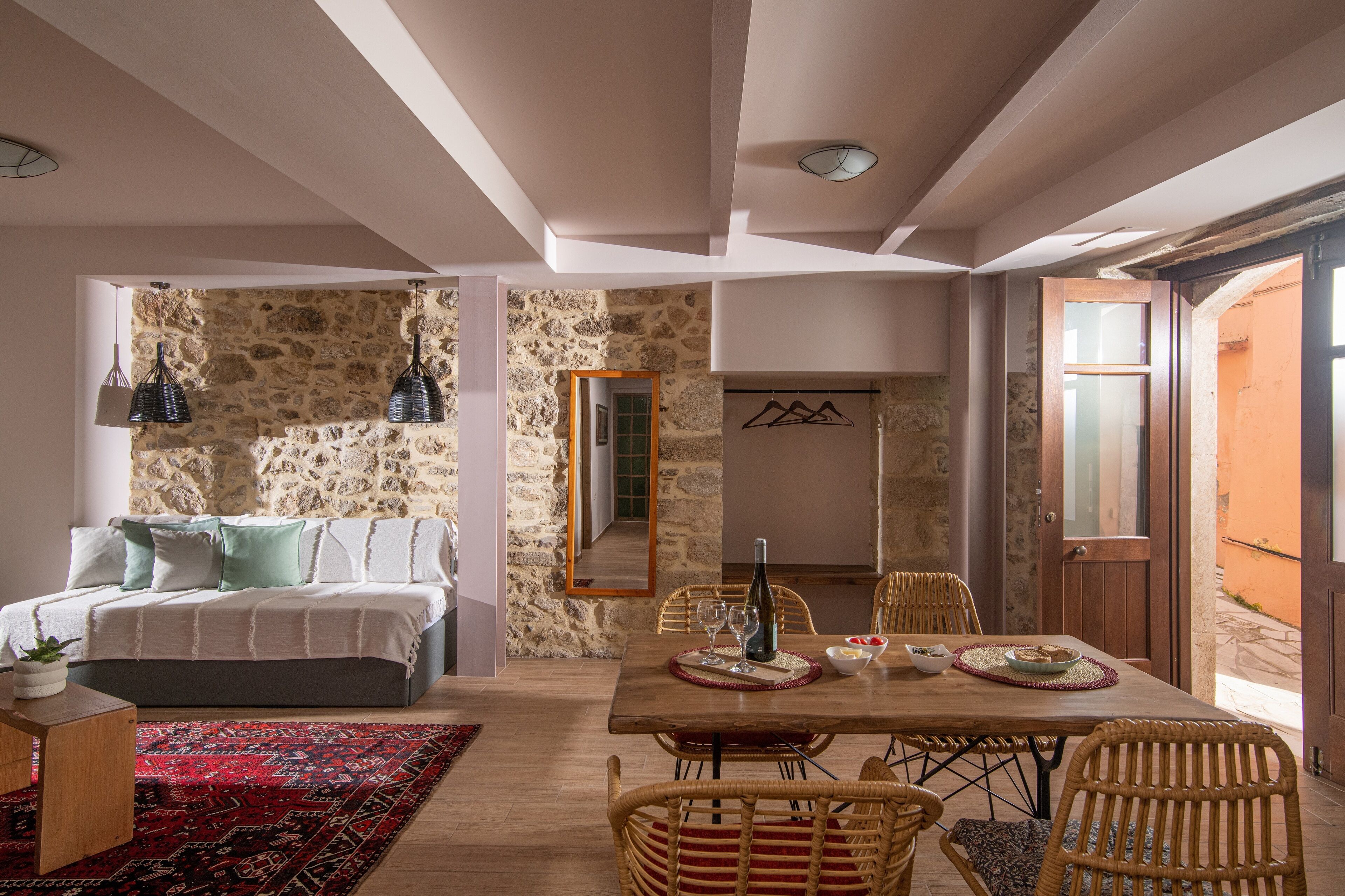 Una habitación acogedora con pared de piedra, una cama con almohadas, una mesa de comedor con sillas y un espejo en la pared.