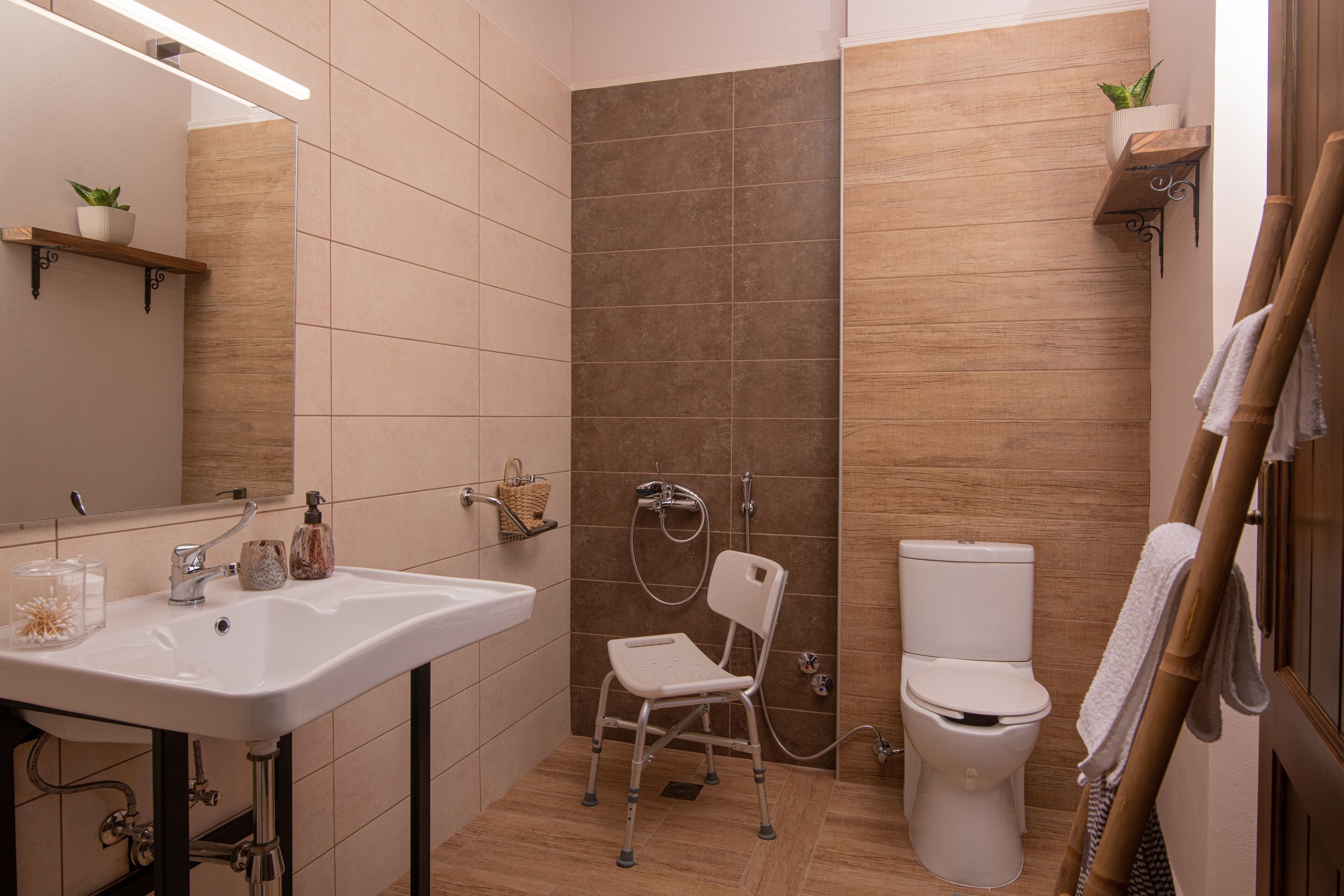 Ein modernes Badezimmer mit einem weißen Waschbecken, einer Dusche inklusive Handbrause, einer Toilette und einem hölzernen Handtuchhalter.